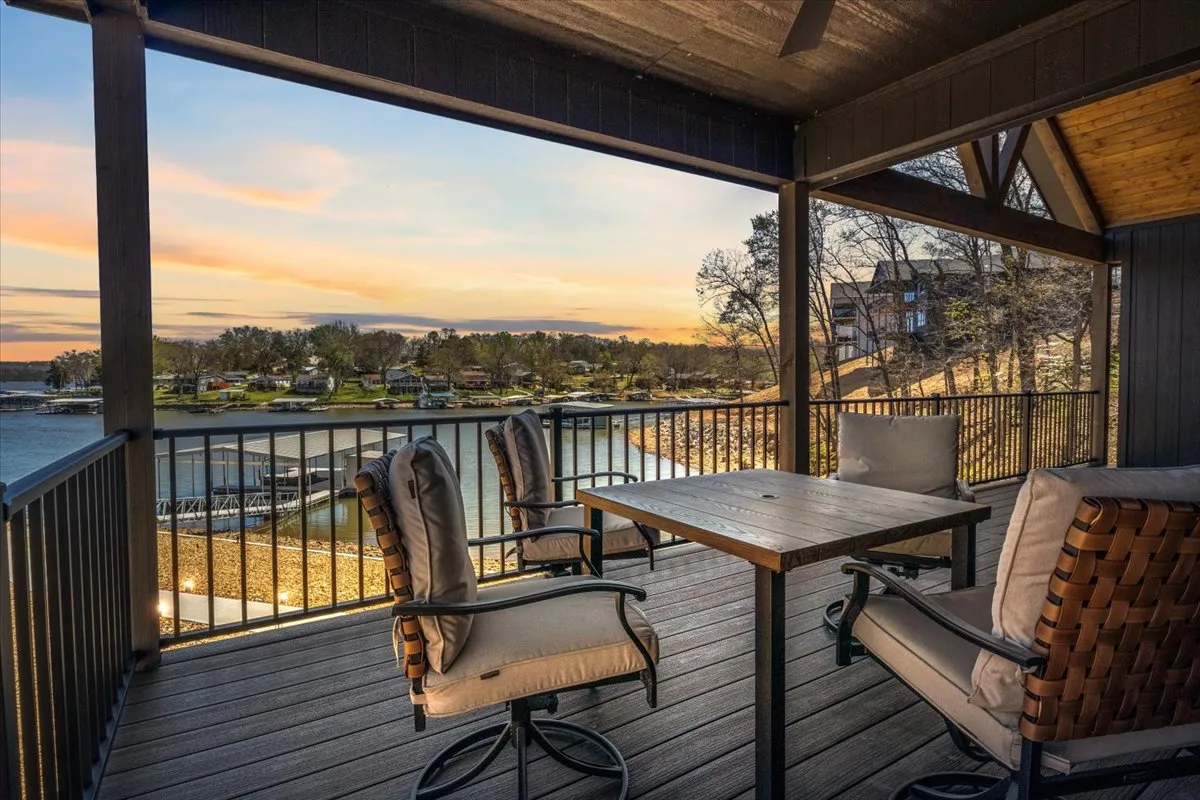 A serene exterior shot showcasing a lake view from the deck, with patio furniture and a wooden railing. The space is set for outdoor dining or relaxing, offering expansive water views and a peaceful ambiance ideal for gatherings.
