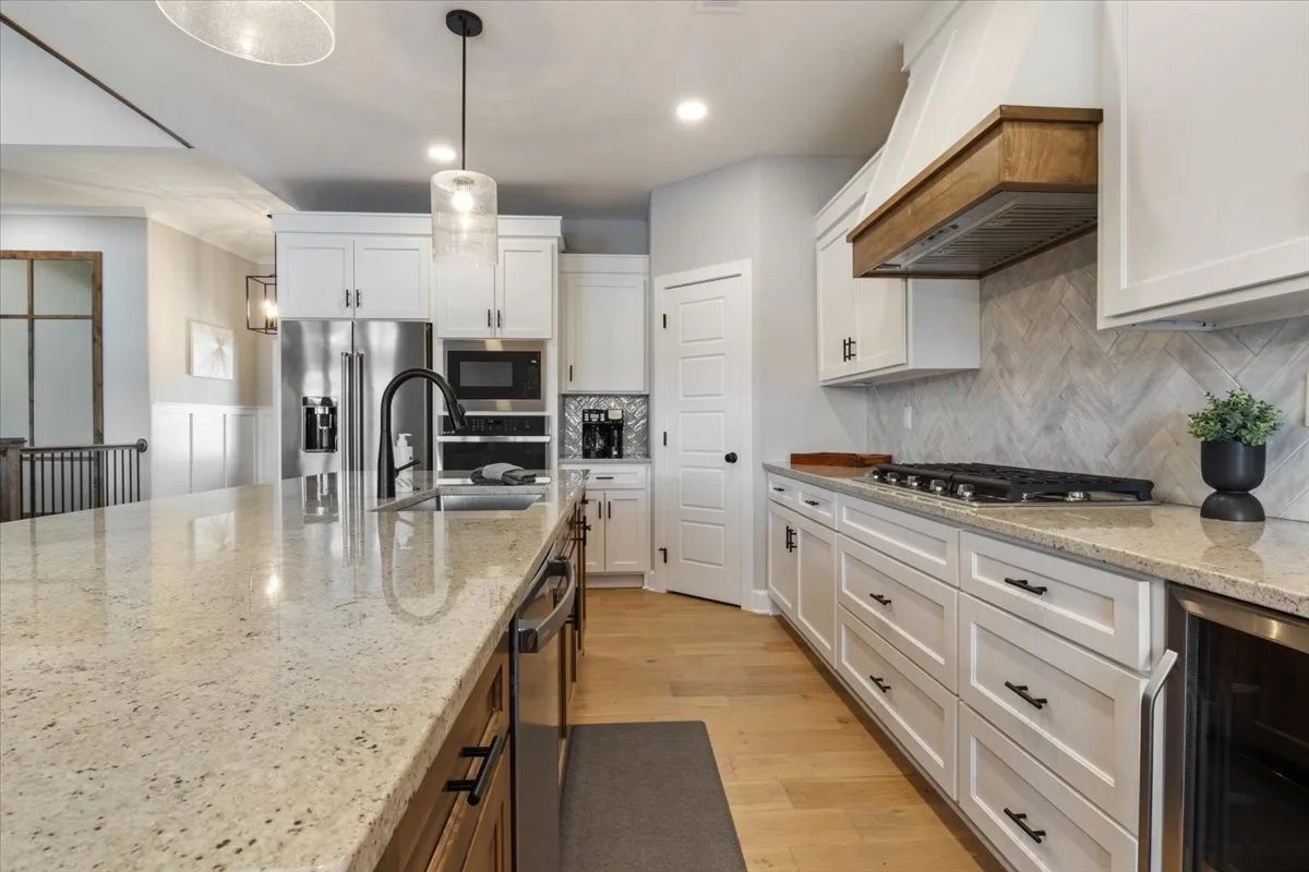 This image showcases a large kitchen island with stainless steel appliances, white cabinetry, and a herringbone backsplash. The scene is well-lit and designed for cooking and entertaining, with ample space for family gatherings and meal preparation.