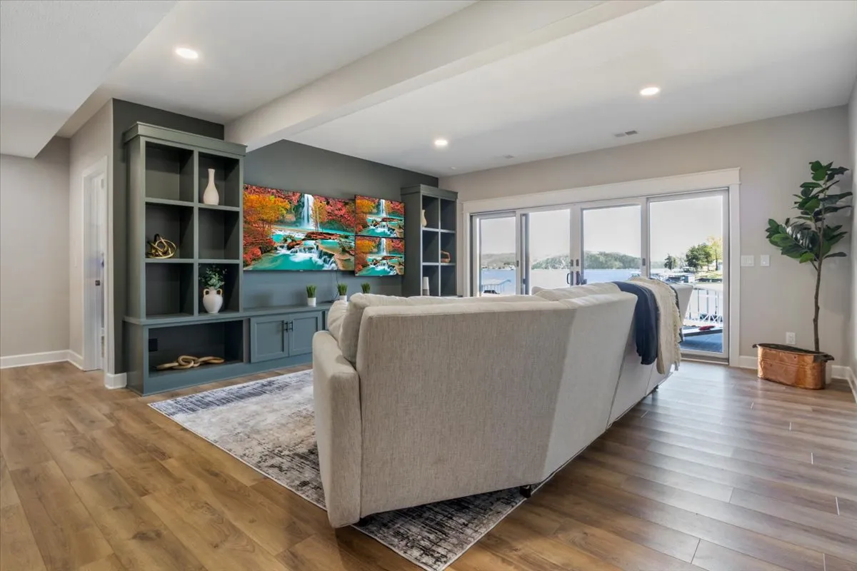 A tranquil living area with a comfortable sofa facing a large screen TV displaying a nature scene. Decorative shelving and large windows overlooking the water amplify the cozy, relaxed mood of the space, ideal for gatherings or quiet moments.