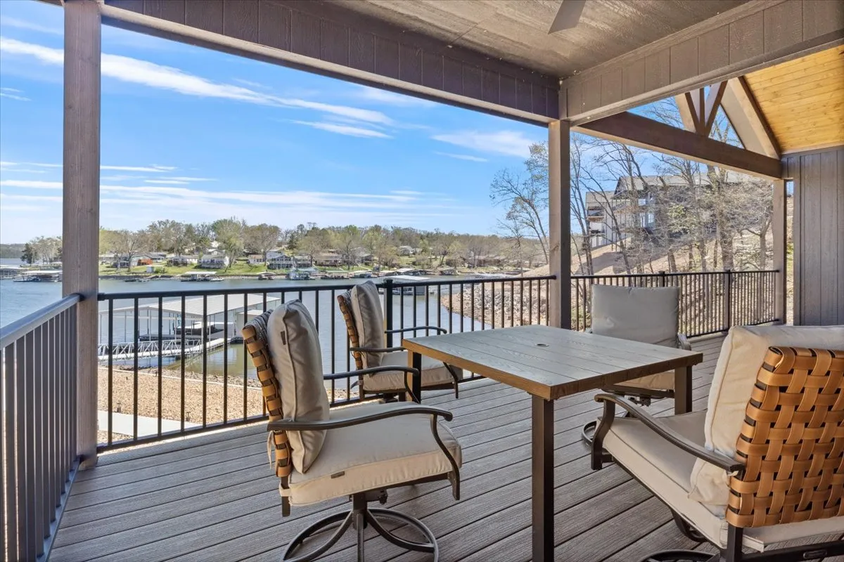 The image focuses on a tranquil outdoor seating area overlooking the lake, with distant houses dotting the shoreline. This inviting space suggests moments of relaxing, socializing, and watching boats pass by, reinforcing the lakeside lifestyle and opportunities for waterfront dining or leisure.