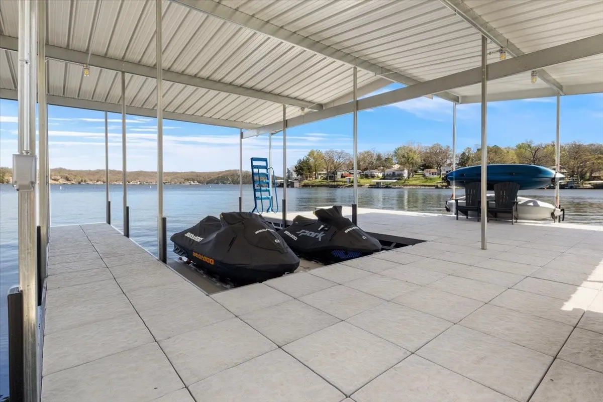 A dock extends into the lake with jet skis anchored nearby, offering expansive views of the water and sky. The scene is both adventurous and peaceful, illustrating private access to water activities and moments of relaxation on the dock.