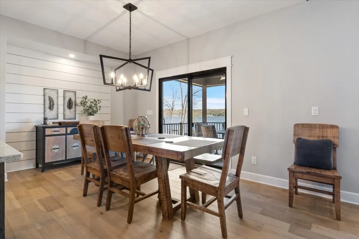 A cozy dining area featuring a large wooden table, a striking chandelier, expansive windows, and tasteful decorative wall art. The setup is inviting for both family feasts and intimate breakfasts.