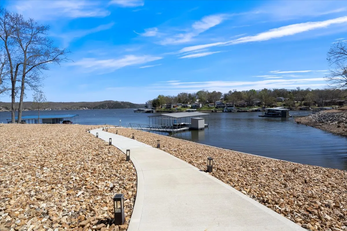 A gentle, zero-step pathway leads from the house toward the lake, passing trees and boathouses along the way. The path is inviting and accessible, visually emphasizing the easy, stair-free transition from indoors to the waterfront.