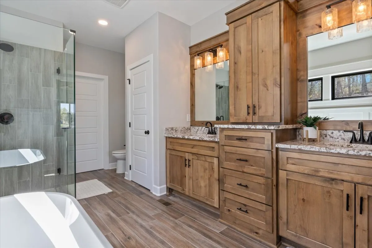 A modern bathroom featuring a freestanding bathtub, double vanity with large mirrors, and a spacious glass shower enclosure. Bright natural light streams in, and the space is step-free, echoing nearly ADA-compliant design for accessibility and comfort.