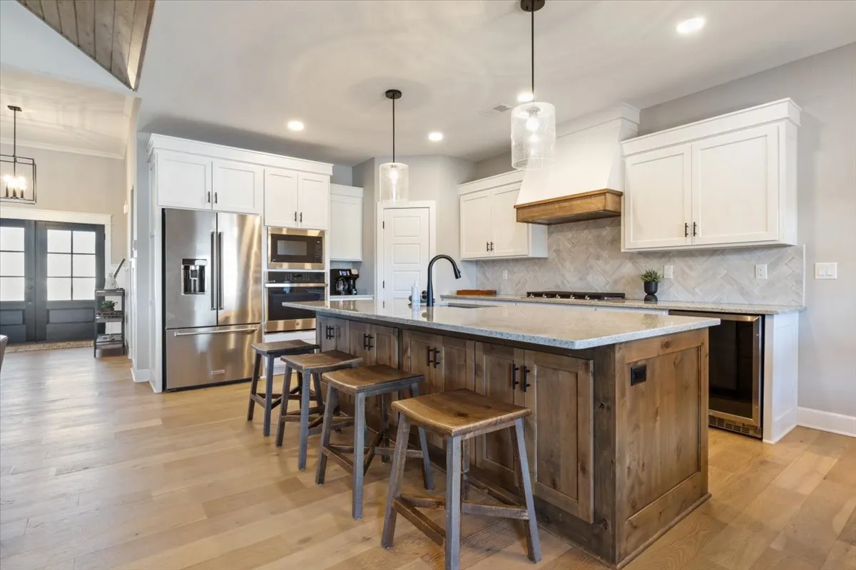 The image captures a vibrant kitchen scene with a central island, stools, and modern appliances, set up for both cooking and entertaining. The mood is warm and welcoming, with signs of baking and family activities.