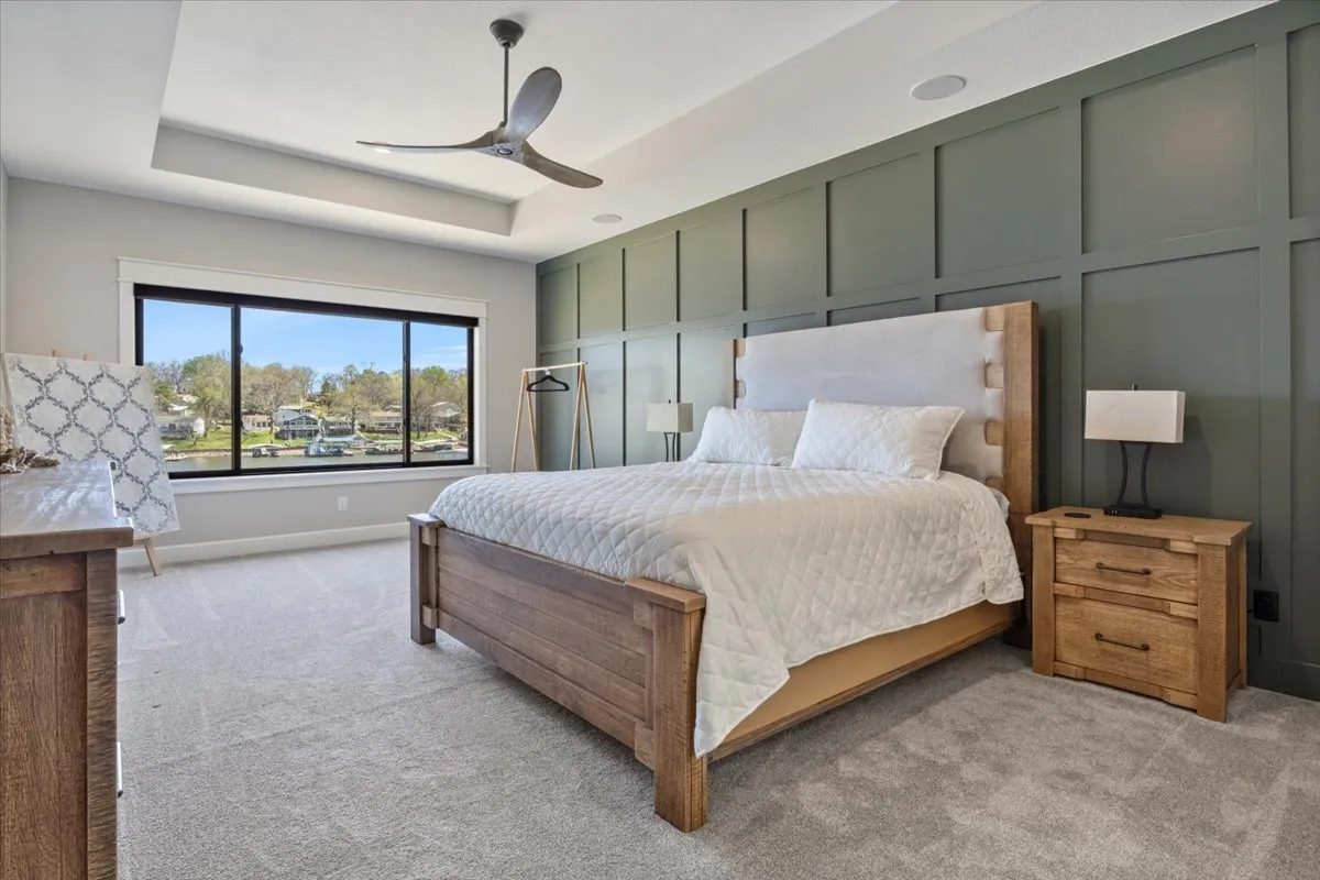 A serene bedroom featuring a king-sized bed with plush bedding, wooden nightstands on each side, a large window flooding the room with natural light and offering scenic views, and a ceiling fan overhead. The atmosphere is tranquil and inviting, ideal for rest and relaxation after a day of adventure.