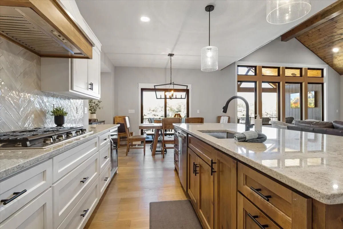 A wide view of the kitchen island and the connected dining area, bathed in natural light from large windows. The space is arranged for family gatherings and entertaining guests, with visible seating and open layouts.