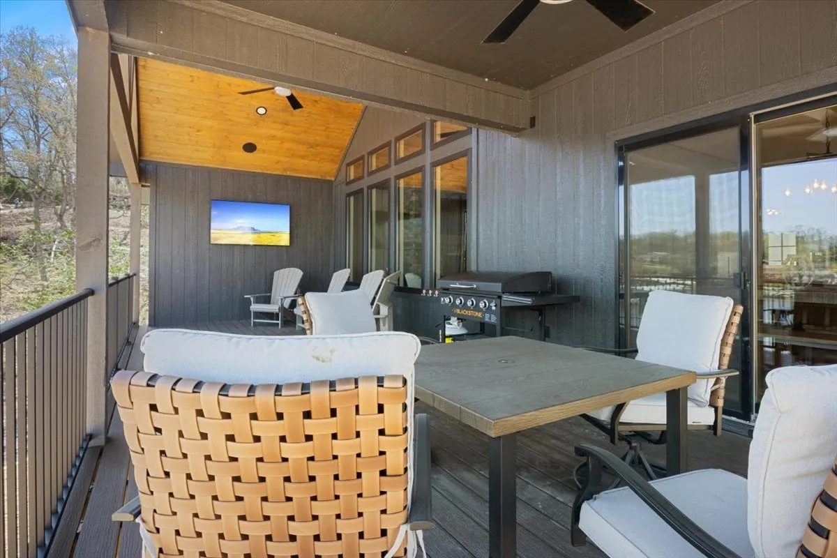 This image showcases an outdoor seating area with a grill station, outdoor television, table, and comfortable furniture arranged for social gatherings. The lake is visible in the background, with a tranquil atmosphere perfect for entertaining or relaxing. The space is designed for easy access and seamless flow between indoor and outdoor living.