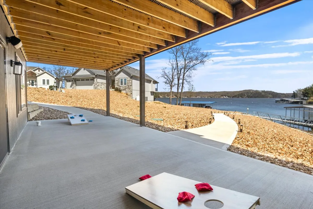 An inviting exterior scene featuring a waterfront view, the home's architecture, and a cornhole game setup. The area is ideal for outdoor recreation, socializing, and enjoying the scenic backdrop, supporting the playful aspect of the section.